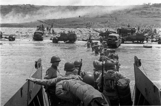 U.S. troops wade ashore from an LCVP landing craft, off "Omaha" Beach, on D-Day, 6 June 1944. Note DUKWs and half-tracks at the water line, lines of men headed inland, and M1903 and M1 rifles carried by some of the troops leaving the landing craft. Official U.S. Army Signal Corps photo.