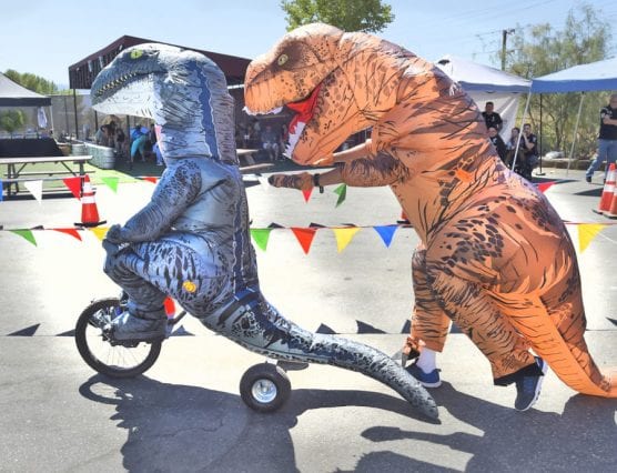 Wolf Creek Brewery teammates Joson Lester, left, riding his trike in a dinosaur suit, gets a push from Scott Wesselhoff as they compete during the Child & Family Center's 3rd annual Trike Derby held at Wolf Creek Brewery in Santa Clarita on Saturday, September 21, 2019. | Photo: Dan Watson/The Signal.